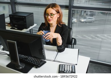 Pretty, nice, cute, perfect woman sitting at her desk on leather chair in work station, wearing glasses, formalwear, having laptop and notebook on the table - Powered by Shutterstock