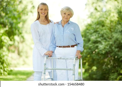 Pretty nurse and senior patient with walking frame looking at camera outside
