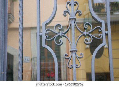 Pretty old wrought iron work catches the light. The glass behind reflects the colours in the street. Smart and elegant, protective bars in the centre of town. Stone doorways and neutral street colours