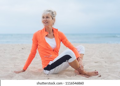 Pretty Older Blond Woman Relaxing On A Beach In Sportswear Turning To Look Back Over Her Shoulder Watching Something