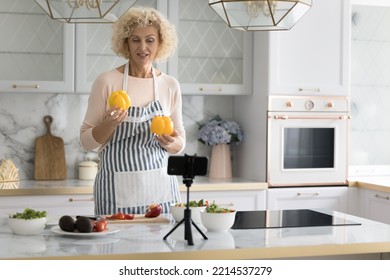 Pretty Older Woman In Apron Holds Yellow Paprika Talks About Healthy Balanced Eating, Record Vlog On Cellphone Camera, Films Cooking Video Vlog For Internet Channel, Vlogging, Cookery On-line Class