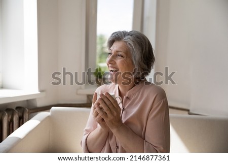 Pretty overjoyed 50s woman holds teacup smile looks into distance enjoy teatime sit on cozy sofa in warm living room, relish favourite beverage spend morning at home. Carefree retiree portrait concept