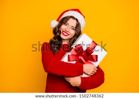 Pretty overjoyed lady holding large giftbox close to chest wear knitted jumper and santa hat isolated yellow background