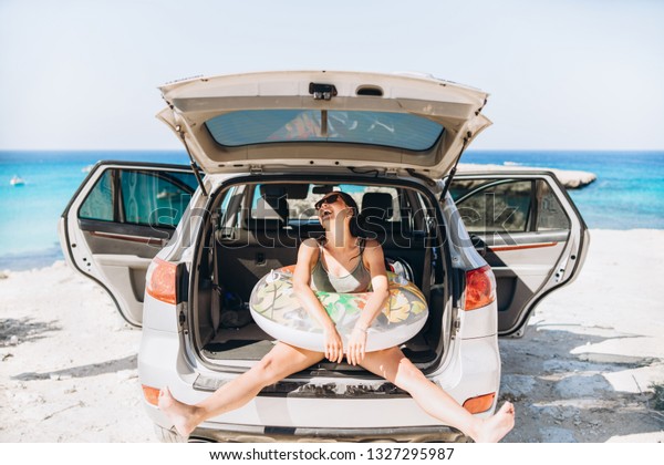 Pretty pan asian brunette with float near car trunk\
at the seaside beach