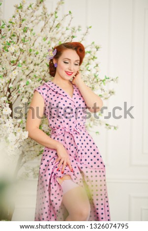 pretty pin up girl in retro polka dot dress near tree with white flowers
