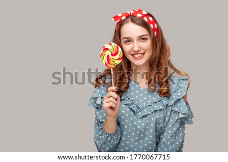 Pretty pinup girl ruffle blouse holding sweet spiral candy looking at camera, smiling with delicious confectionery lollipop in her hands. retro vintage style. studio shot isolated gray background,