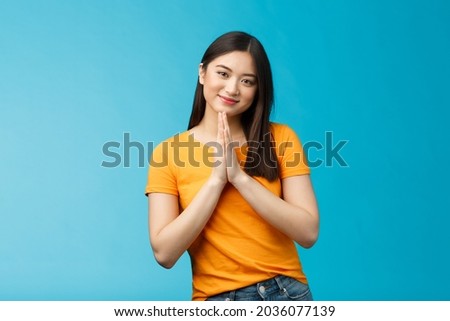 Pretty please girl asking politely. Cute charming asian woman smiling tenderly, hold hands pray grinning begging for favour, plead, look thankful for help stand blue background joyful, caring