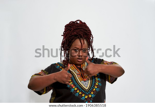 Pretty plump young haitian woman showing shaka\
gesture and looking at camera while posing on white background.\
Emotions and feelings\
concept