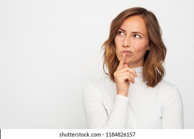 Pretty portrait of young beautiful woman and adult thinking looking left and smiling a bit having a finger at her lips, isolated on white background
					