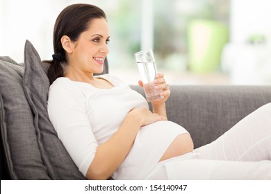 pretty pregnant woman drinking water while lying on a sofa at home - Powered by Shutterstock