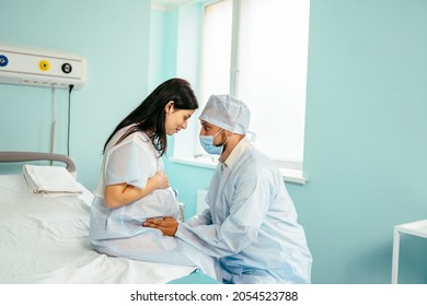 Pretty pregnant woman sitting on medical couch while lovely husband gently embracing her tummy. Happy young couple preparing for birth of firstborn ar modern clinic. Parenting and support concept. - Powered by Shutterstock