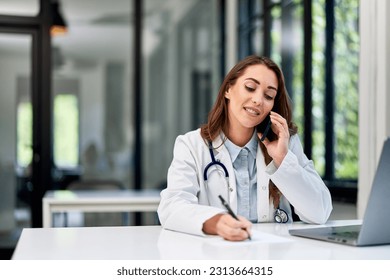 A pretty professional female doctor sitting at the ambulance table, taking notes while having a phone call. - Powered by Shutterstock