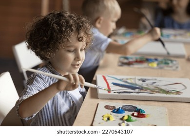 Pretty pupil kid boy painting on class, studying art in artistic school for children, drawing abstract picture on canvas at table, using paintbrush, palette with oil, acrylic paints - Powered by Shutterstock