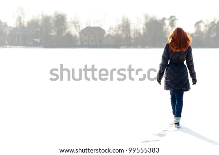 Pretty red haired girl walking on frozen lake and making footpath