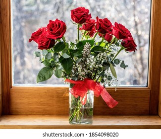 Pretty Red Roses In A Glass Vase With A Red Bow Sitting In A Window With A Snowy View Outside.