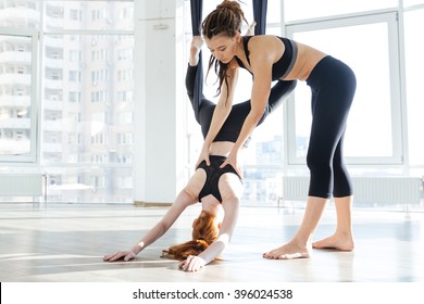 Pretty redhead girl practicing aerial yoga with personal trainer in studio