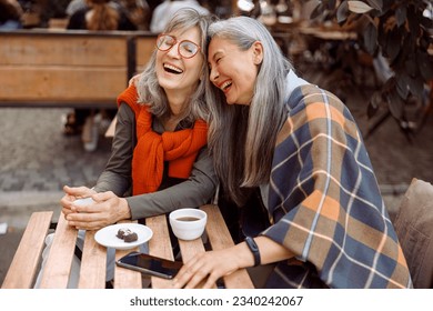 Pretty senior Asian woman puts head on laughing friend shoulder resting together at table in street cafe on nice autumn day - Powered by Shutterstock