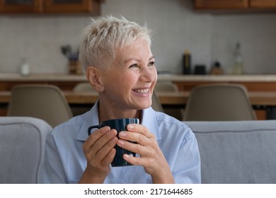 Pretty senior blonde woman sit on couch holds mug laughs staring into distance looks joyful, spend carefree leisure alone at home, enjoy morning coffee in kitchen. Start new day, feeling good concept - Powered by Shutterstock