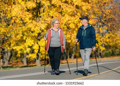 Pretty Senior Couple With Nordic Walking Poles In Colorful Autumn Park. Mature Woman And Old Man Resting Outdoors.