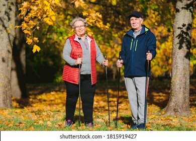 Pretty Senior Couple Standing With Nordic Walking Poles In Colorful Autumn Park. Mature Woman And Old Sportman Resting Outdoors. 