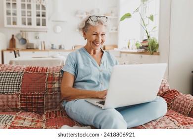 Pretty senior woman in denim home clothes video chatting online with her friend or relatives, spending leisure time on sunday relaxing on sofa using laptop, smiling looking at screen - Powered by Shutterstock