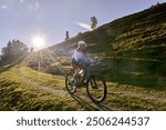 pretty senior woman riding her electric mountain at sunset in the Allgau alps below the Nagelfluh mountain chain next to Steibis, Bavaria, Germany 