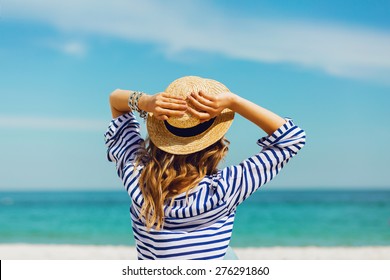  Pretty Slim Tan  Blonde Stylish Woman In Straw Hat  And Sunglasses. Posing On The Paradise Tropical Beach. Have Bright Mace Up And Wearing Striped Shirt. 
