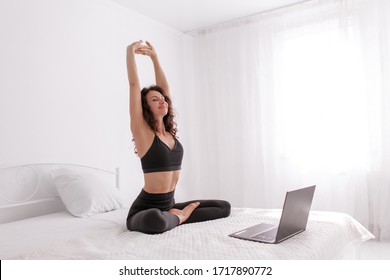 Pretty slim woman doing yoga online infront of laptop in bedroom. Stay home concept.