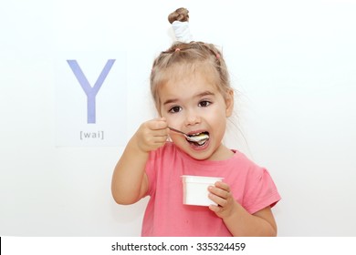 Pretty small girl eating a yogurt over white background with Y letter on it, indoor portrait