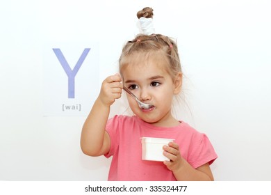 Pretty small girl eating a yogurt over white background with Y letter on it, indoor portrait