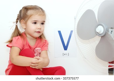 Pretty small girl sitting near the electric fan (ventilator) over white background with V letter on it, indoor portrait, ABC concept