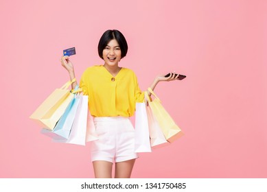 Pretty Smiling Asian Woman With Shopping Bags Showing Credit Card In Hand Studio Shot Isolated On Pink Background