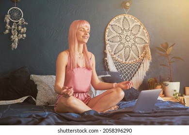 Pretty Smiling Female Model Meditates Near Laptop On Large Bed By Dark Blue Wall