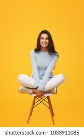 Pretty smiling woman in stylish clothes sitting on chair against orange background. 