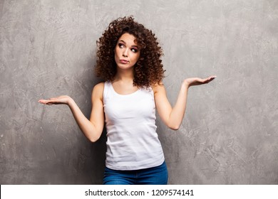 Pretty Smiling Woman In White T-shirt Isolated On Gray Background Asking You To Make A Choice Between Two Products