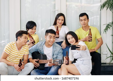 Pretty Smiling Young Asian Woman Taking Selfie With Friend Playing Guitar At House Party