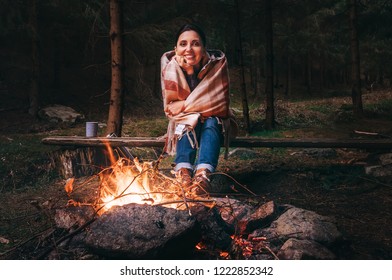 Pretty Smiling Young Woman Sits Near The Campfire In Twilight Autumn Forest