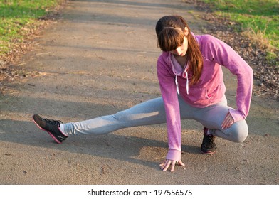 Pretty Sporty Brunette Woman Athlete Stretching Her Legs After A Run Over The Park. On A Bright Sunny Day, At Sunset