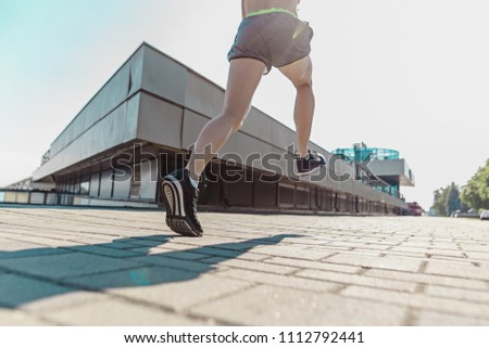 Pretty sporty woman jogging at city at morning. Fit fitness young caucasian girl running. Female sports model in summer sunny day exercising outdoor. Feet close up
