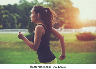 Pretty sporty woman jogging at park in sunrise light - Shutterstock ID 302420963