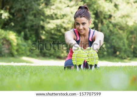 Pretty sporty woman stretching sitting on the ground smiling at camera