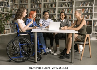 Pretty student girl with disability sits in wheelchair talking to interracial schoolmates, studying together, joking, laughing, make joint project, engaged in teamwork having good friendly relations - Powered by Shutterstock