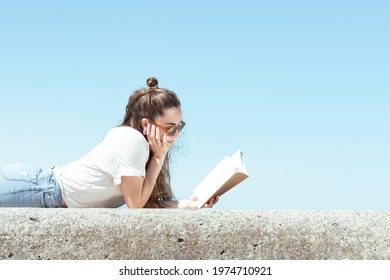 Pretty student reading a book and studying outdoors in a sunny summer day. - Powered by Shutterstock