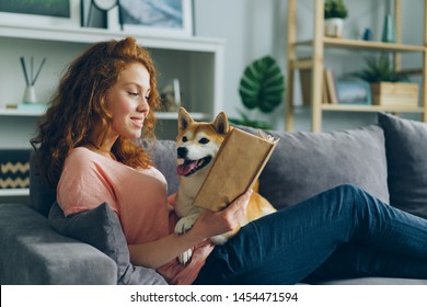 Pretty student young woman is reading book in cozy apartment smiling and petting adorable dog sitting on comfy couch at home. Animals and hobby concept. - Shutterstock ID 1454471594