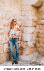 A pretty stylish girl posing in jeans, a shirt with flower ornament, vintage shoes and glasses in front of a wall - Shutterstock ID 385843555
