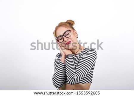 Pretty stylish young woman in striped shirt posing isolated on grey wall background studio portrait. People lifestyle concept. Sleeping with folded hands under cheek