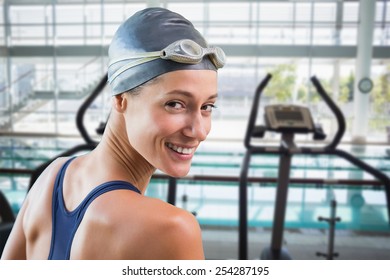 Pretty swimmer by the pool smiling at camera against cross trainer machines overlooking large swimming pool