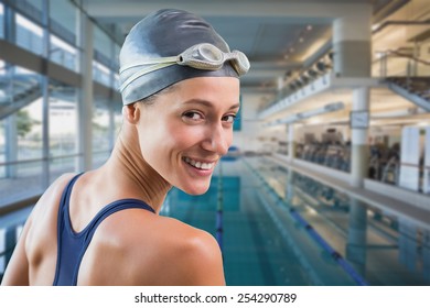 Pretty swimmer by the pool smiling at camera against empty swimming pool with large windows
