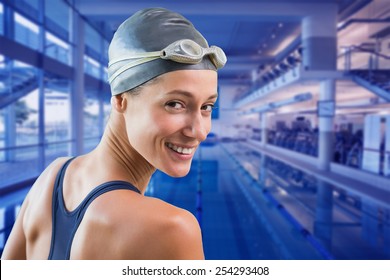 Pretty swimmer by the pool smiling at camera against empty swimming pool with large windows
