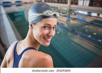 Pretty swimmer by the pool smiling at camera against empty swimming pool with lane markers